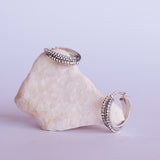 Orecchini doppi a cerchio in oro bianco con due file di cristalli bianchi appoggiati su una pietra bianca su sfondo lilla