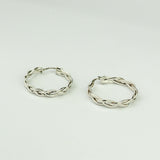 Orecchini in oro bianco a treccia a cerchio su sfondo verde chiaro